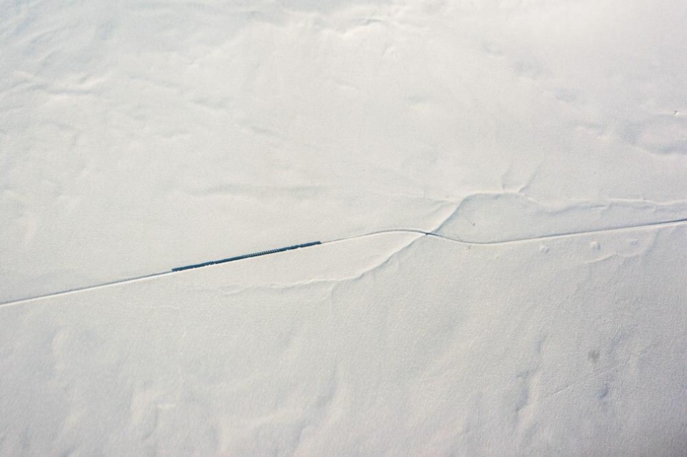 Un tren cruzando camino en medio de la nieve, visto desde la ventana de un avión. 